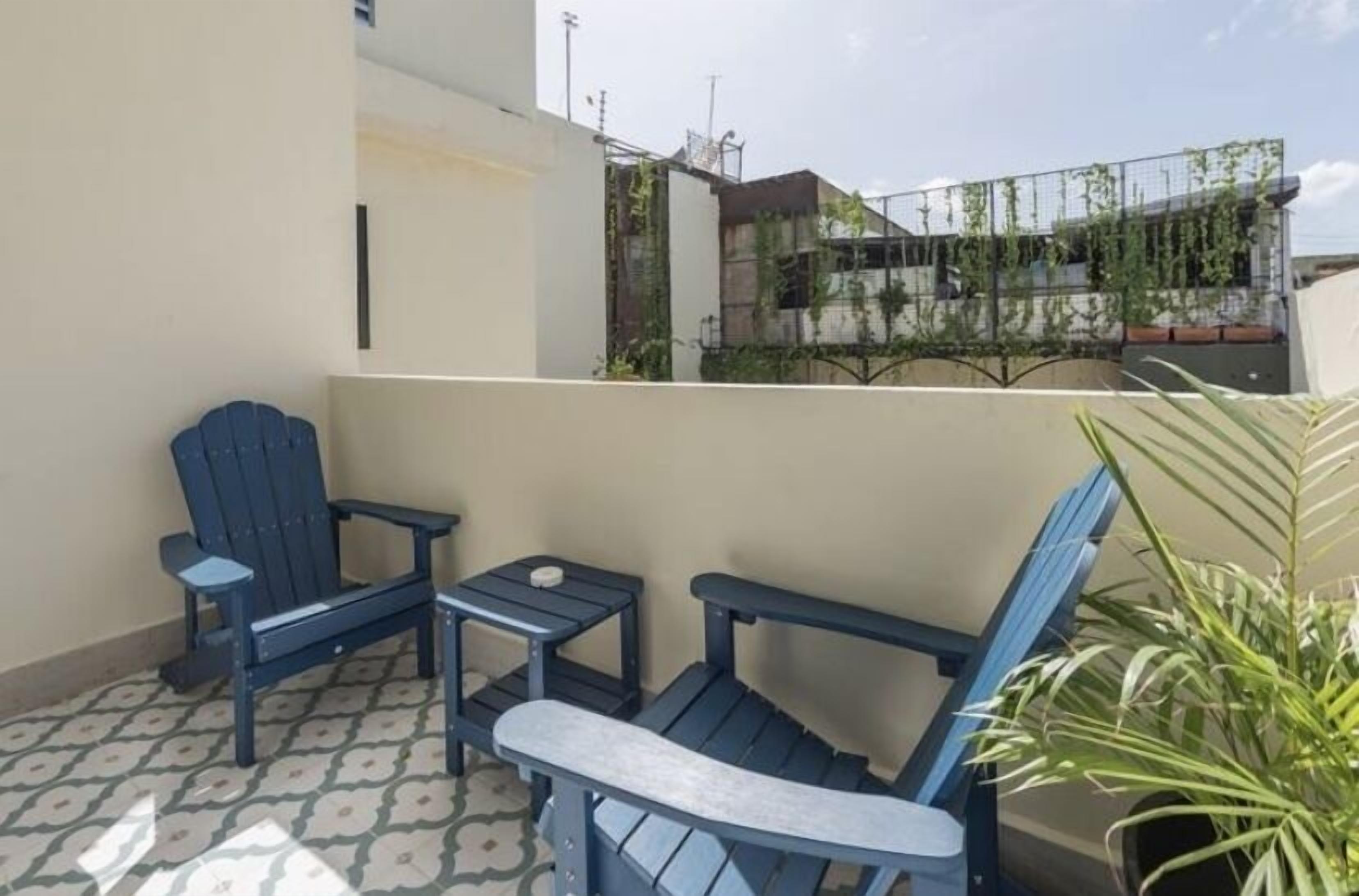 Un balcone con due sedie blu, un tavolino, una pianta in vaso e un pavimento decorato.