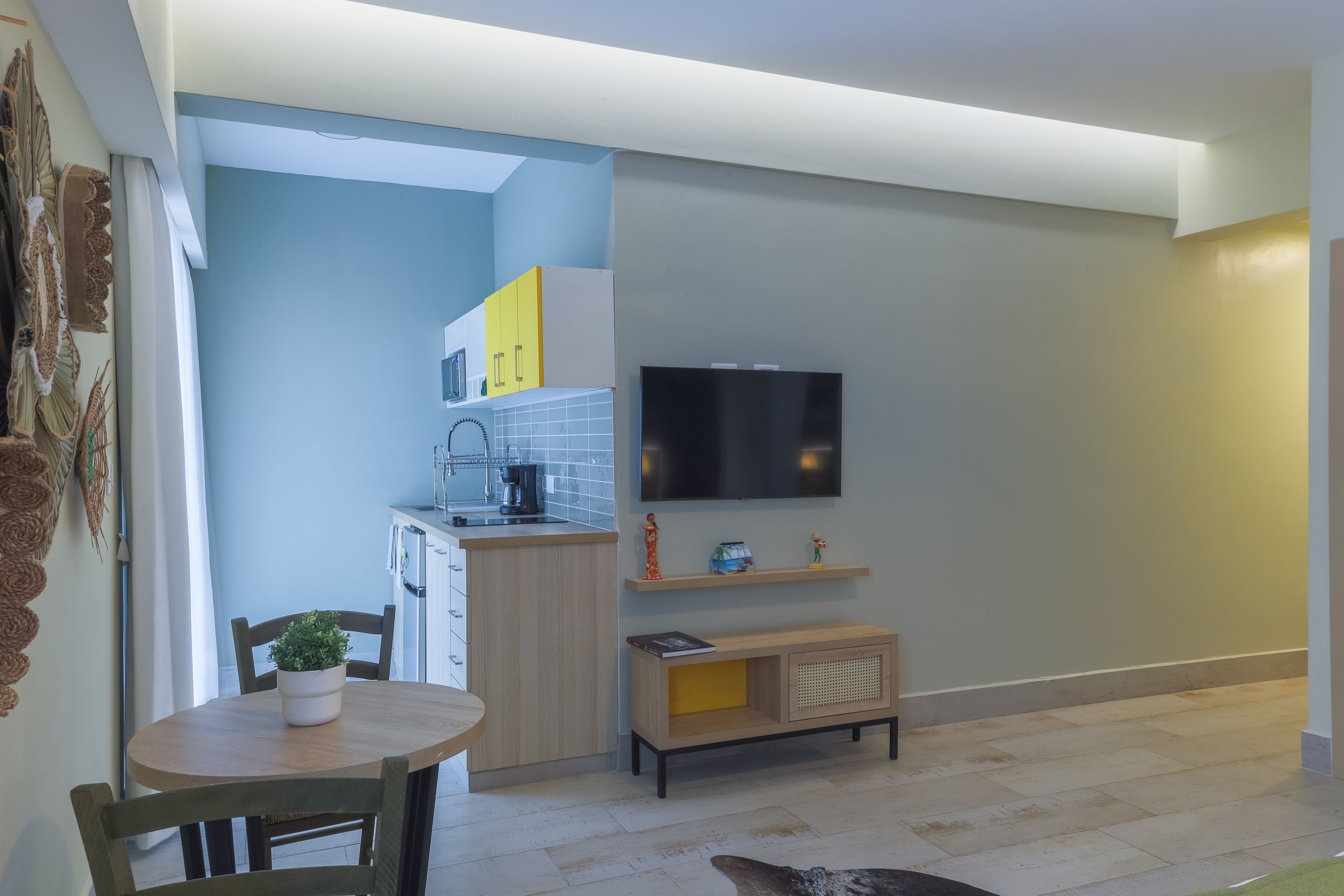 Eine moderne Küche mit Einbauofen, Mikrowelle und Spüle. Ein Esstisch mit Stühlen und ein Topf mit Pflanze sind ebenfalls vorhanden. Ein Flachbildfernseher ist über der Arbeitsplatte an der Wand montiert.