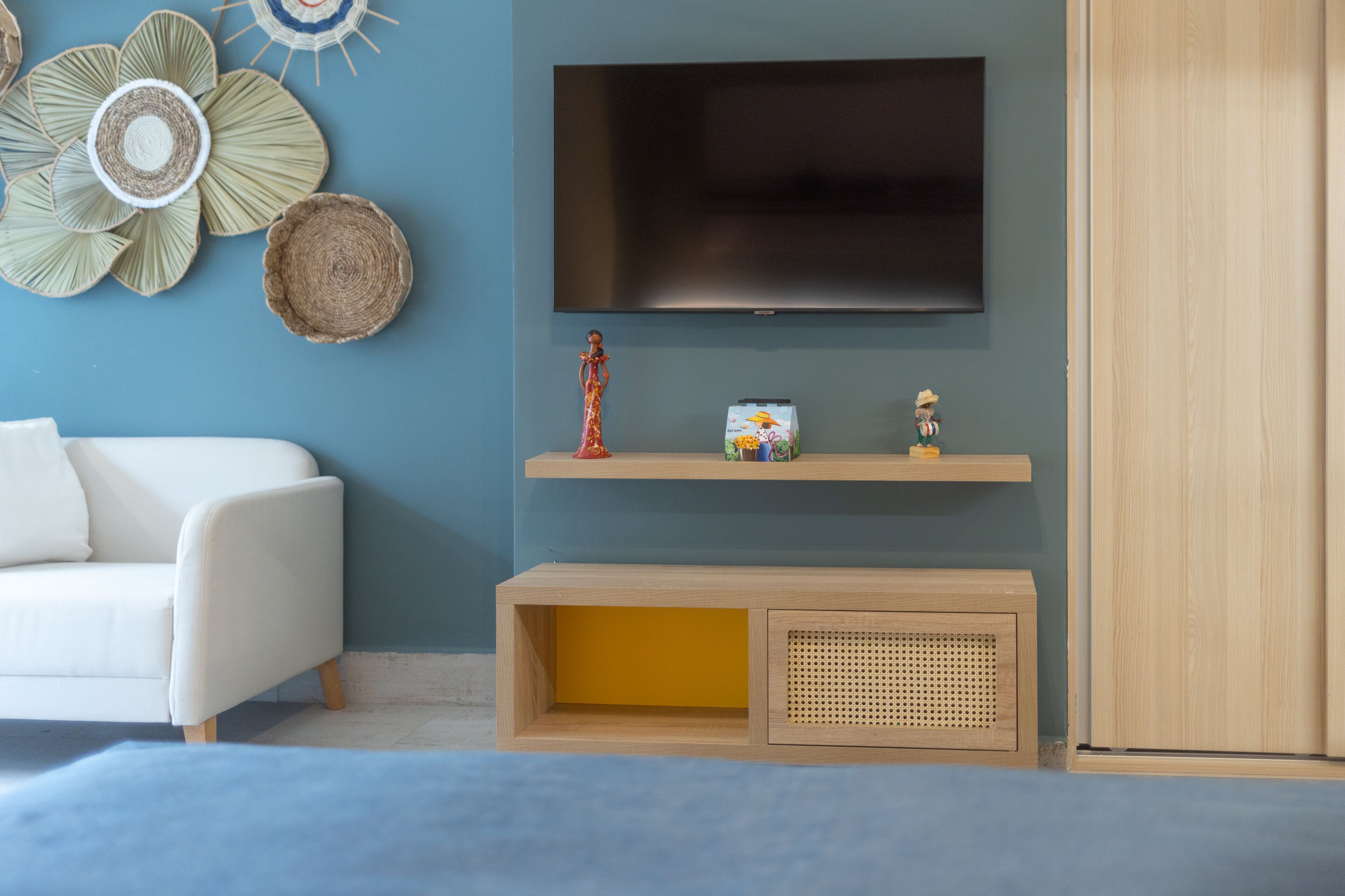 Een moderne woonkamer met een flatscreen televisie aan de muur, een witte bank, een houten console en decoratieve objecten, en een houten garderobe.