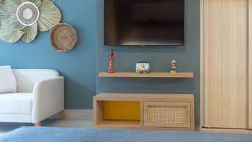 Een moderne woonkamer met een flatscreen televisie aan de muur, een witte bank, een houten console en decoratieve objecten, en een houten garderobe.