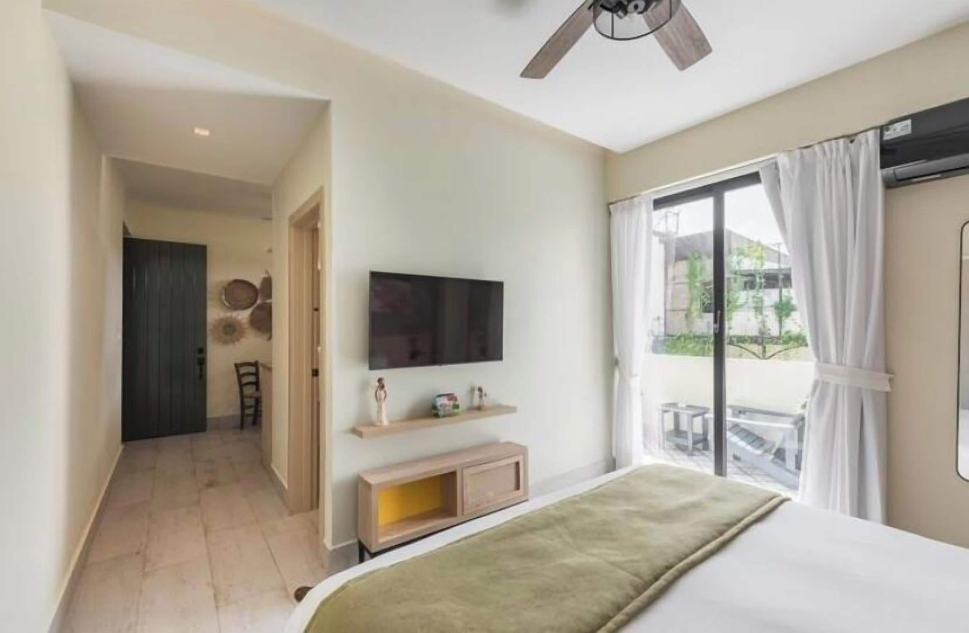 A hotel room with a bed, a TV mounted on the wall, a small console table, and a window with curtains.