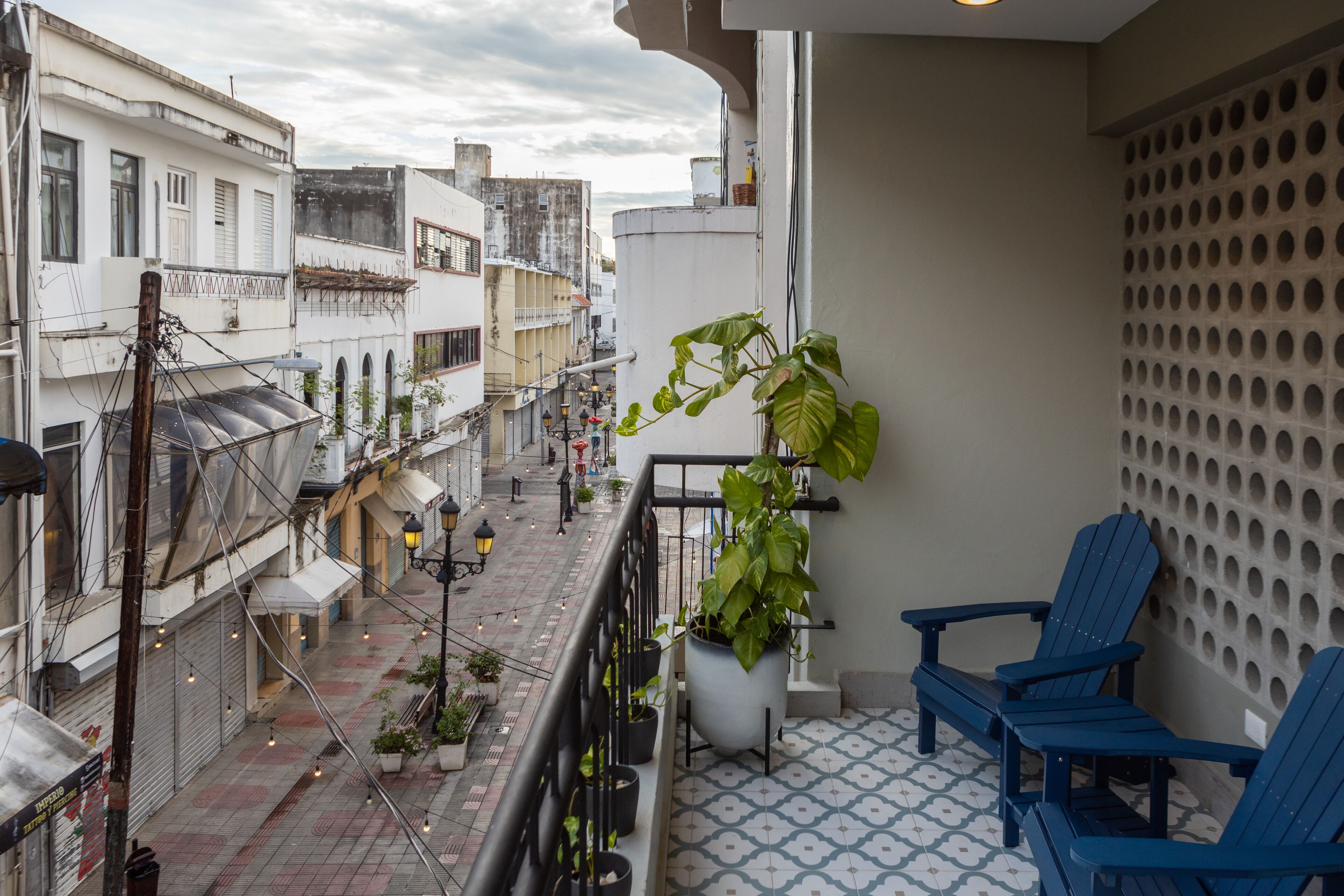 A balcony with potted plants, blue chairs, and a patterned floor.