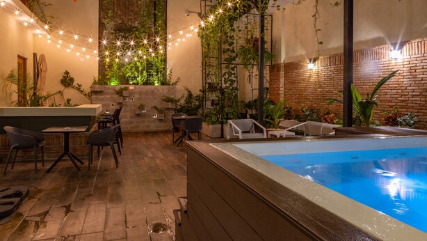 An indoor pool area with a brick wall, string lights, and lounge chairs. - Casa Adefra Boutique Hotel Zona Colonial (Santo Domingo)