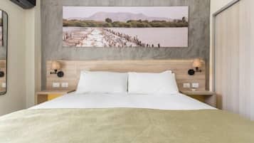 Quarto de hotel com uma cama grande, cabeceira de madeira, duas mesas de cabeceira com luminárias e um quadro de paisagem grande na parede.