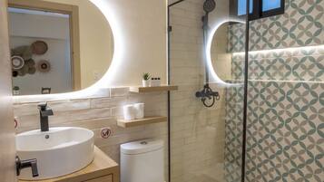 A modern bathroom with a round sink, a toilet, and a glass shower enclosure.
