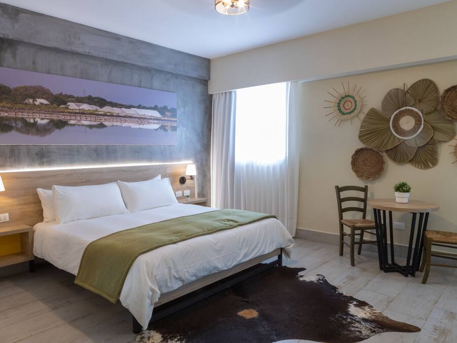 A modern hotel room with a large bed, a view of a lake, a dining area with a table and chairs, and decorative wall art.