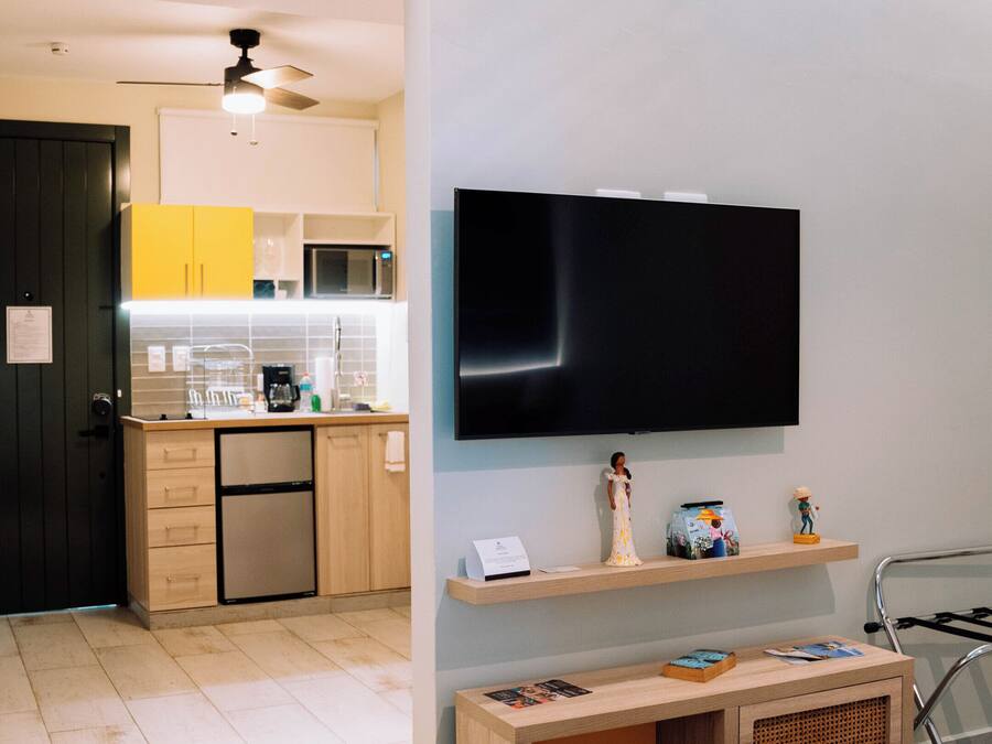 Ein modernes Wohnzimmer mit einem flachbildfernseher an der Wand, einem Holzkonsolentisch mit Zeitschriften, einem Lederteppich und einer im Hintergrund sichtbaren Küche.