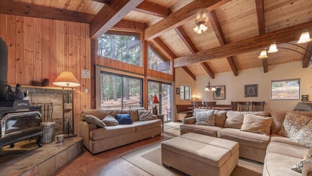 Un intérieur de chalet chaleureux avec des murs en bois, de grandes fenêtres, une cheminée et des sièges confortables.