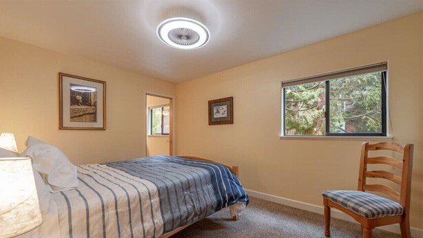 Un dormitorio con una cama individual, una silla, una lámpara y una ventana con vistas a árboles.