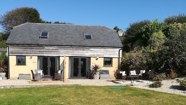 Une maison à deux étages, dotée d’un toit en pente, de grandes fenêtres et d’un patio aménagé avec du mobilier d’extérieur.