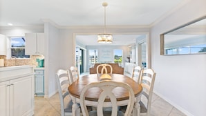 A modern kitchen with white cabinets, a dining table with six chairs, and a chandelier.