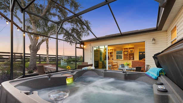 A hot tub with a glass seat, surrounded by a covered patio with a view of a house.