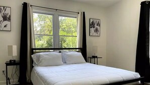 A neatly made bed with white bedding in a room with a black metal frame. There are two bedside tables with lamps, and a window with curtains.