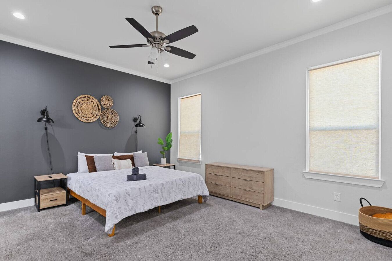 A bedroom with a bed, bedside tables, a ceiling fan, a dresser, and a window with blinds.