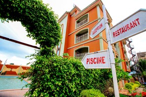 A building with signs for a restaurant, reception, and a pool. - Benin Metropole Hotel (Parakou)
