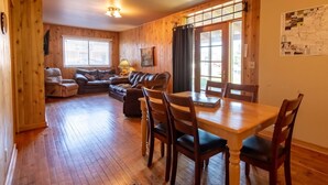 A cozy room with a wooden interior, a dining table with chairs, a sofa set, and a window with curtains. - Come explore the Western UP! Located right on the atv and snowmobile trail. (Ewen)