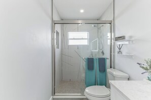 Et moderne badeværelse med en brusekabine i glas, et toilet og en marmorflisebordplade.