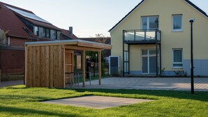 A modern house with a wooden structure in the yard, a balcony, and a clear sky.