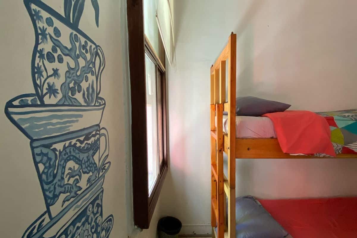A room with a bunk bed, a wall mural, a window, and a door.