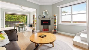 A living room with a fireplace, a television, a coffee table, and a bookshelf. - 2 bedroom tropical beach escape (Bondi Beach)
