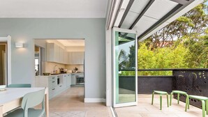A modern kitchen with a dining area, a sliding glass door to a balcony, and a view of greenery outside. - 2 bedroom tropical beach escape (Bondi Beach)