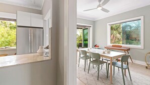 A modern kitchen with a built-in refrigerator, a dining area with a table and chairs, and a large window with a view of greenery. - 2 bedroom tropical beach escape (Bondi Beach)