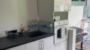 A modern kitchen with white cabinets, a black countertop, a sink, an oven, and a small refrigerator. - AU Jardin D'eden (Le Gosier)