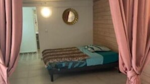 A bedroom with a bed, a round mirror, and pink curtains. - AU Jardin D'eden (Le Gosier)