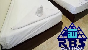 Ett hotellrum med två separata sängar, vita sängkläder, ett nattduksbord med en vas med blommor och en logotyp för RBS Tourism Group på väggen.