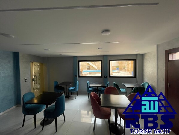 A modern dining area with multiple tables and chairs, large windows with a view of a pool and outdoor area, and a logo for the Tourism Group in the bottom right corner. - King tout pyramid  (Giza)