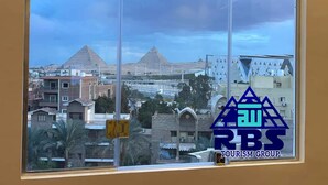 En vy från ett fönster som visar en stadsbild med pyramider i bakgrunden, en klar himmel och logotypen för RBS TOURISM GROUP.