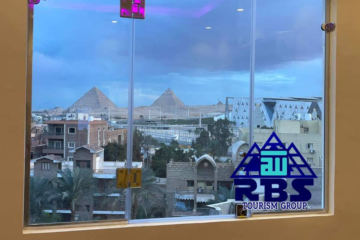A window view of a cityscape with pyramids in the background, a clear sky, and the logo of RBS TOURISM GROUP.