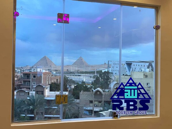 A window view of a cityscape with pyramids in the background, a clear sky, and the logo of RBS TOURISM GROUP. - King tout pyramid  (Giza)