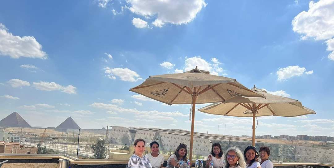 A group of people seated at an outdoor table with a view of pyramids in the background.
