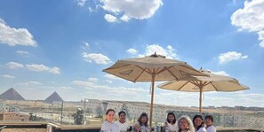 A group of people seated at an outdoor table with a view of pyramids in the background. - King tout pyramid  (Giza)