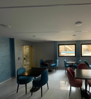 A modern dining area with multiple tables and chairs, large windows with a view of a pool and outdoor area, and a logo for the Tourism Group in the bottom right corner.
