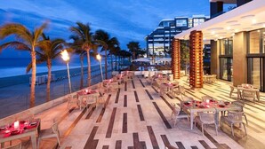 A rooftop bar with tables and chairs, overlooking a beach and the ocean. - Garza Blanca Three Bedroom Loft Los Cabos (Cabo San Lucas)