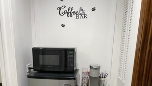 Een kitchenette met een roestvrijstalen koelkast, een magnetron, een koffiezetapparaat en een klein karretje met bestek.