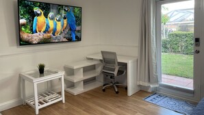 Een kamer met een wit bureau, een stoel, een klein wit bijzettafeltje met een plant en een groot raam met uitzicht op groen.