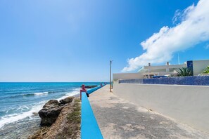 Stroll along the oceanfront walkway, bordered by a blue-painted curb and a white wall.
