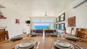 A dining area with a view of the ocean, featuring a wooden table set for four, white walls, and a ceiling fan. - 4 BR Oceanfront Villa with Pool (Isla Mujeres)