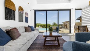 Un salon moderne avec un canapé, une table basse et une vue sur une piscine et un espace de détente extérieur.