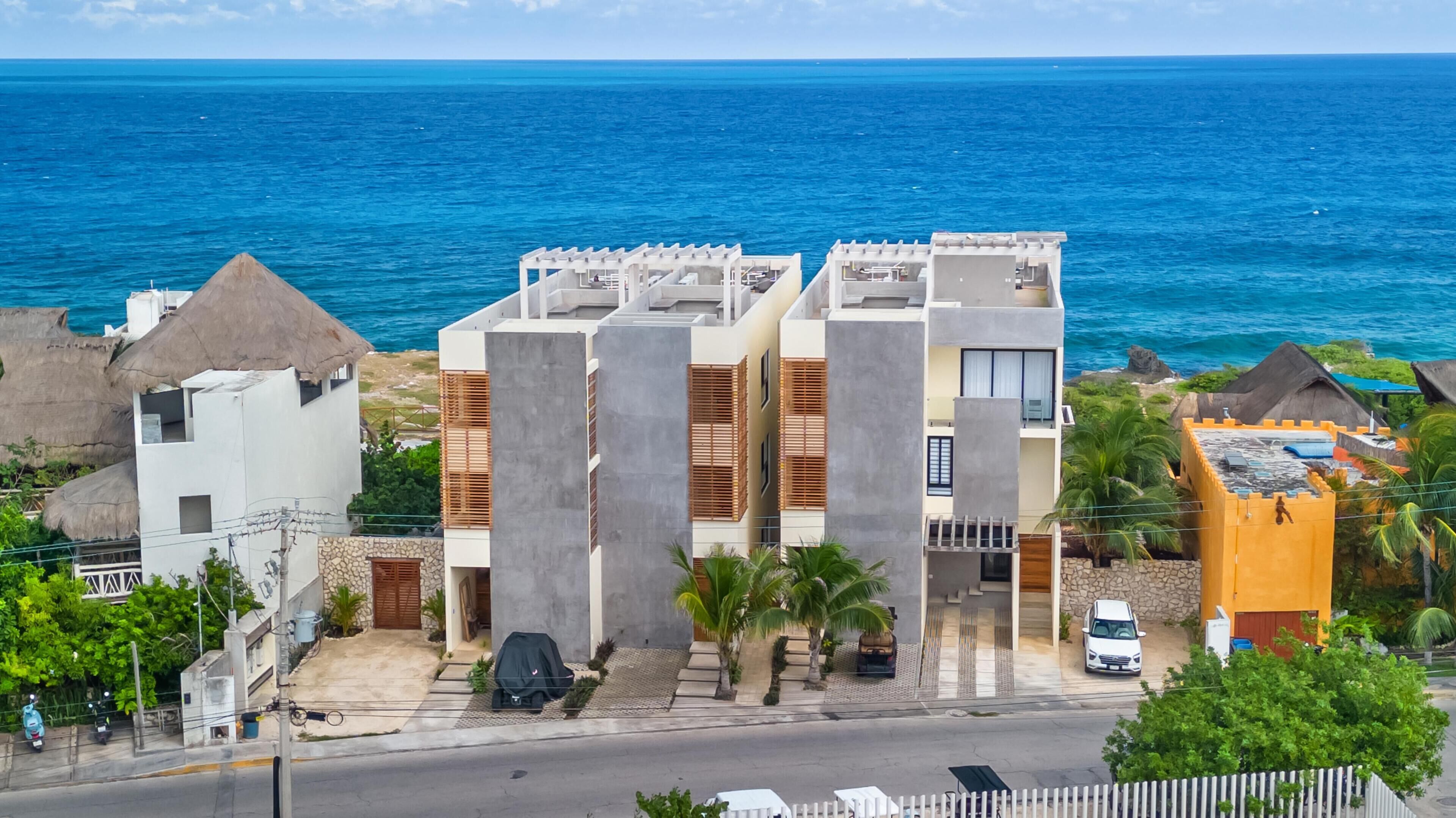 A coastal hotel with a modern design, featuring a central courtyard, a pool, and a view of the ocean.
