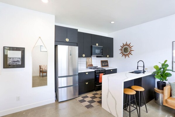 Una cocina moderna con refrigerador, estufa, microondas y taburetes de bar.
