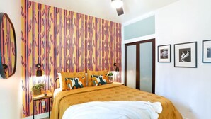 Un dormitorio con cama, ventilador de techo, pared con diseño de cactus y cuadros en la pared.