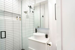 Une salle de bain moderne avec une douche à parois de verre, un lavabo blanc et un miroir au-dessus du lavabo.