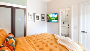 Una camera da letto con un letto, una televisione, una porta del bagno e quadri appesi al muro.