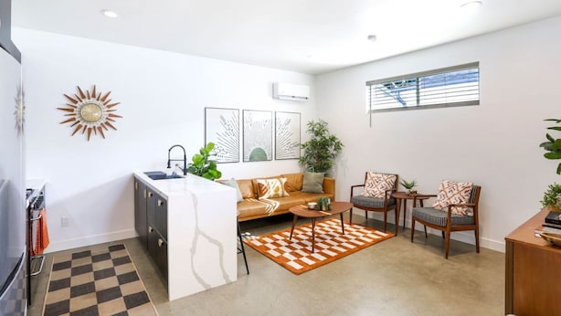 Un espacio habitable compacto con kitchenette, un sofá, dos sillones, una mesa de centro y un amplio ventanal que proporciona luz natural.