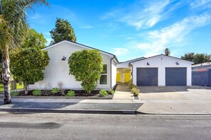 Un bâtiment d’un seul étage, à l’extérieur blanc, avec une porte jaune et un garage à deux portes.