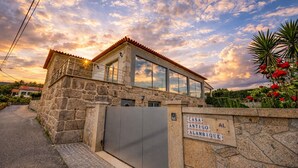 A stone building with a modern glass extension, a metal gate, and a sign reading "CASA ANTIGO ALAMBIQUE".